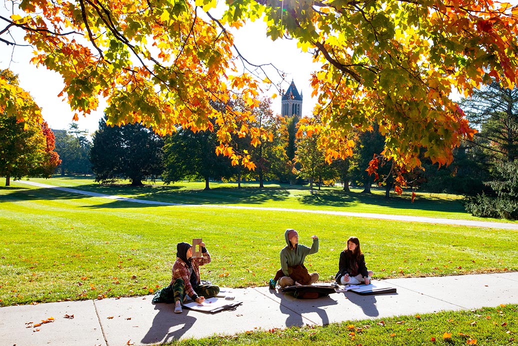 在一个阳光明媚的秋日，三名学生坐在校园中心进行一个项目。
