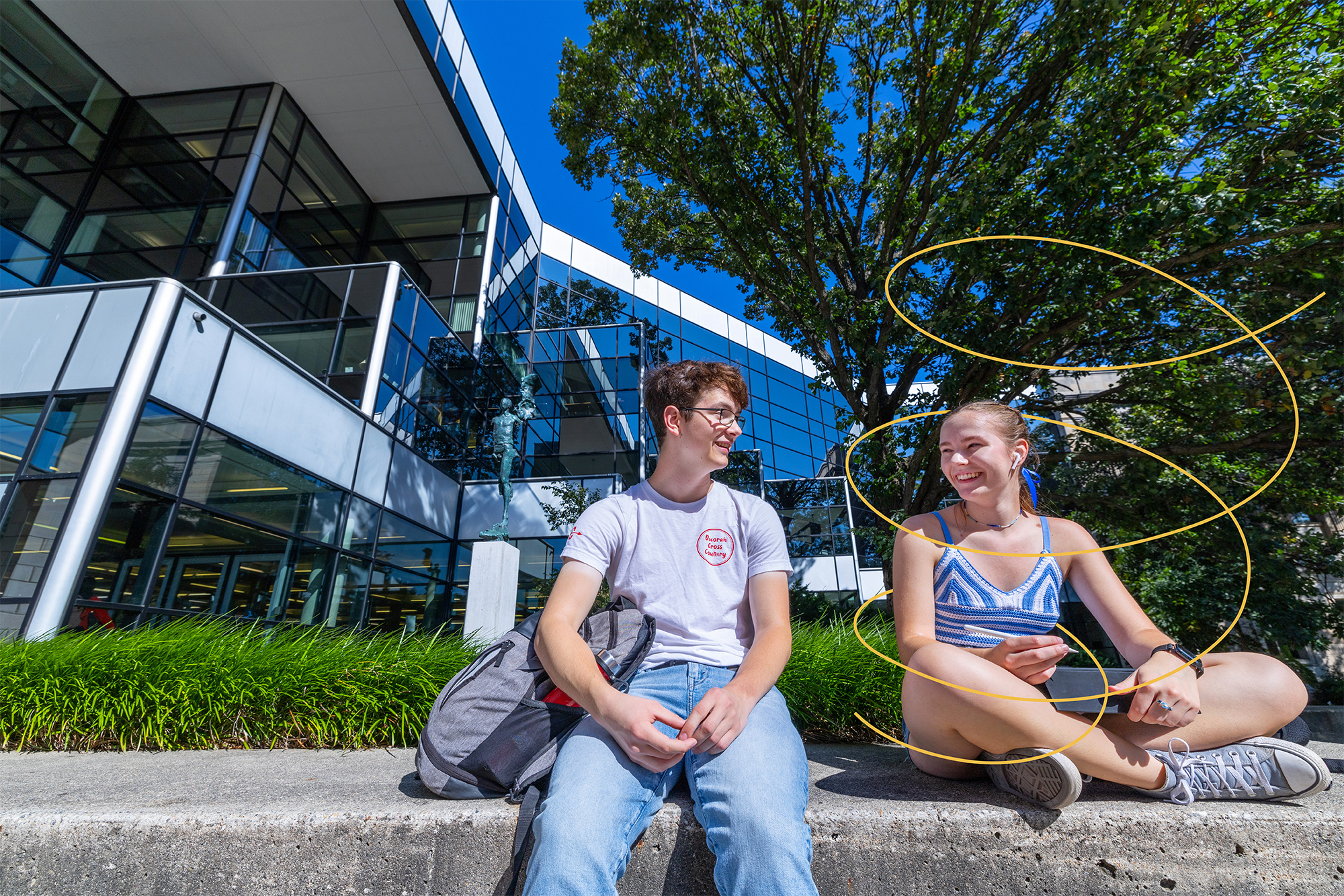 Two students sit outside the library on a sunny day.