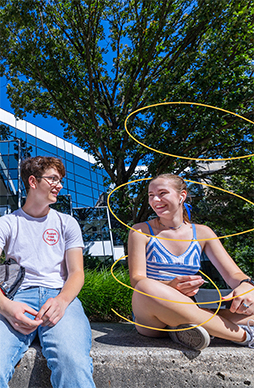 Two students sit outside the library on a sunny day.