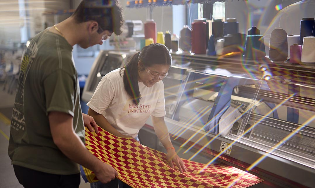 Two students look at a length of cardinal and gold fabric they designed.