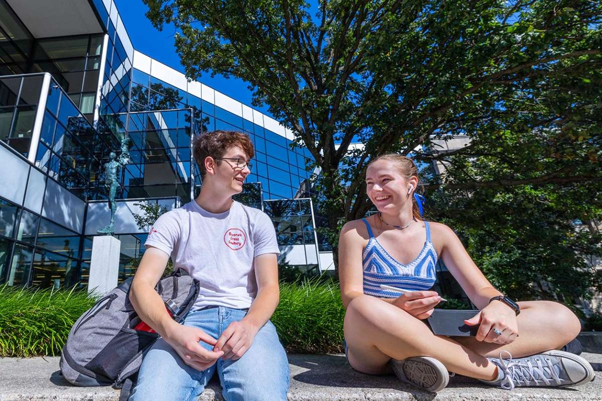 Two students chat outside Parks Library on a sunny summer day.