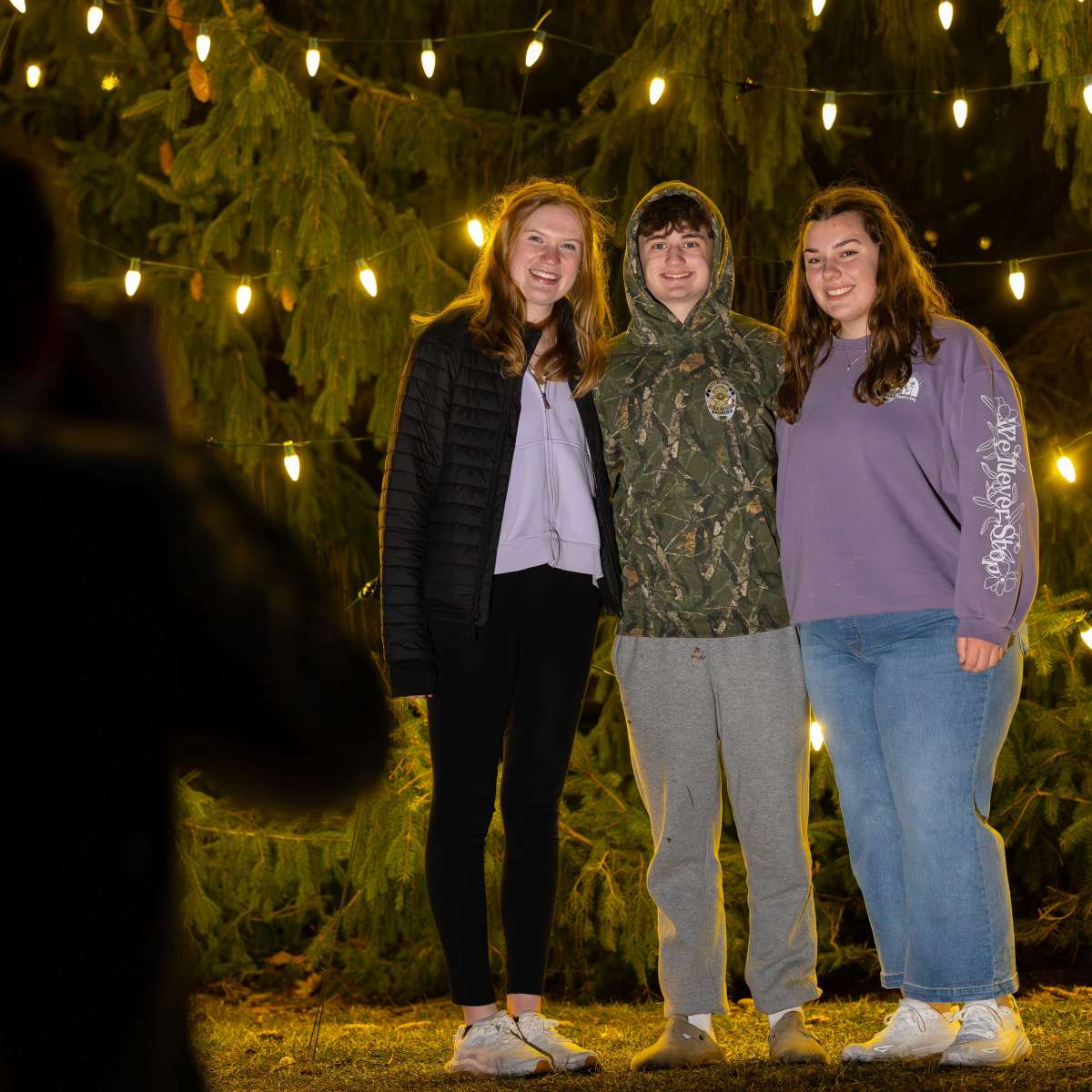 Three Students taking a picture in front of the holiday tree